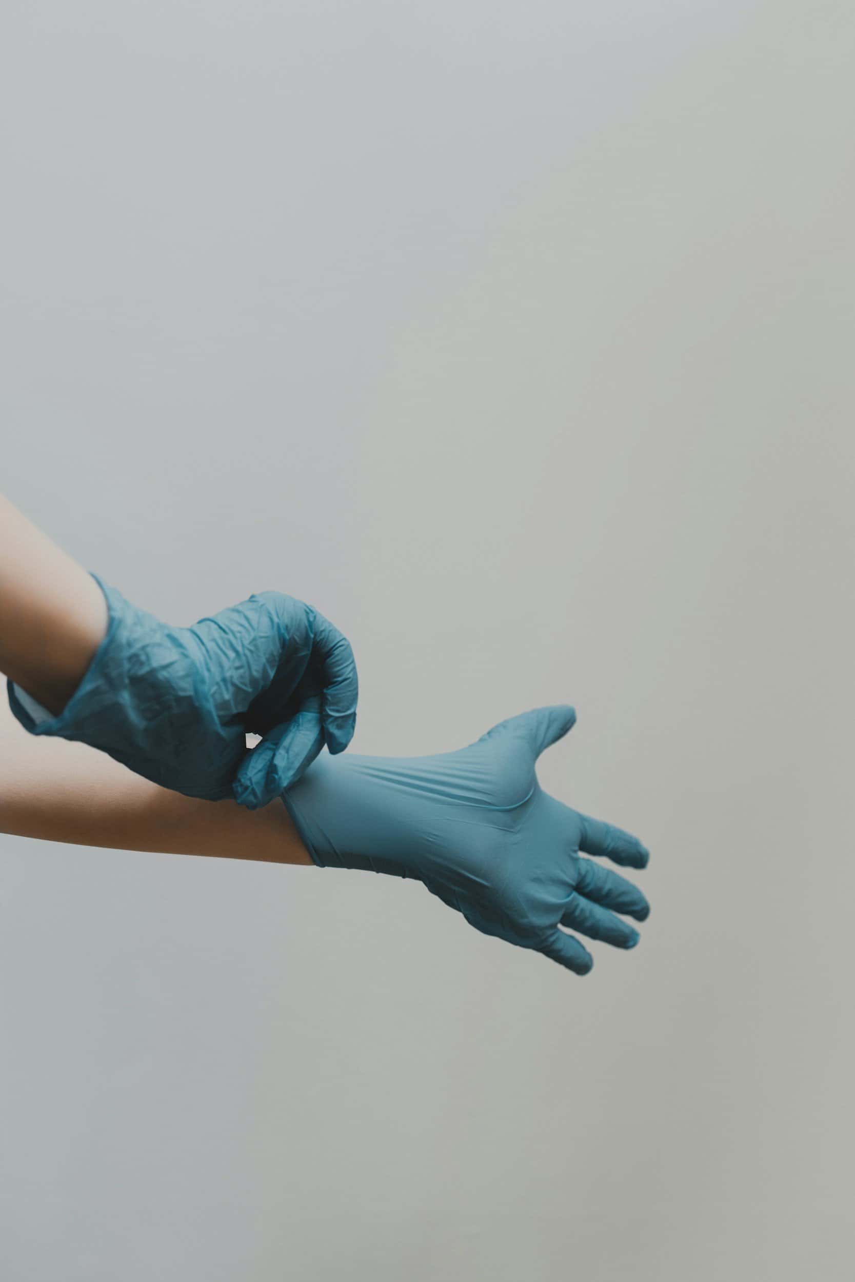 Person putting on blue disposable gloves against a neutral background.